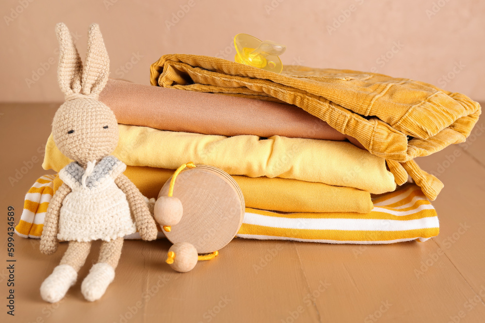 Stack of baby clothes, pacifier and toys on color wooden table