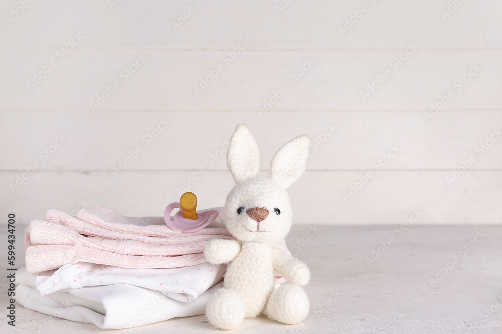 Stack of baby clothes, toy bunny and pacifier on light table