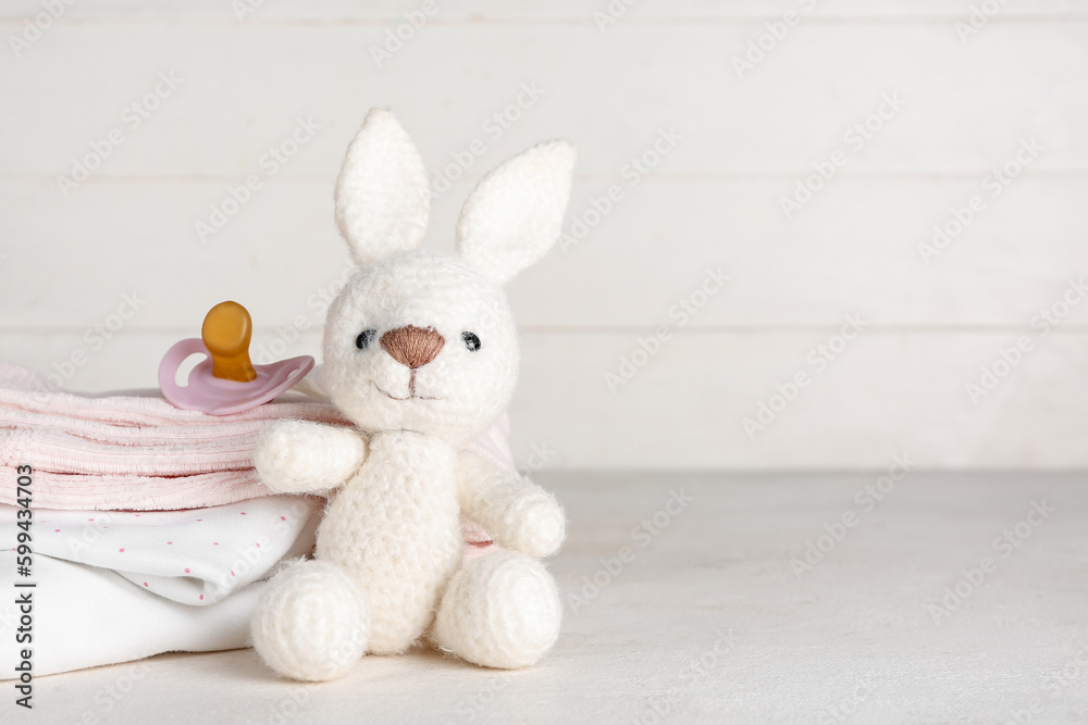 Stack of baby clothes, toy bunny and pacifier on light table