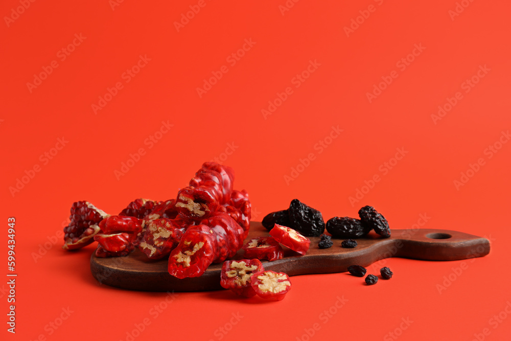 Wooden board with tasty churchkhela, pomegranate, raisin and prunes on color background