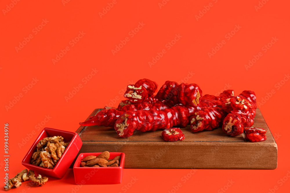 Wooden board with delicious churchkhela and nuts on color background