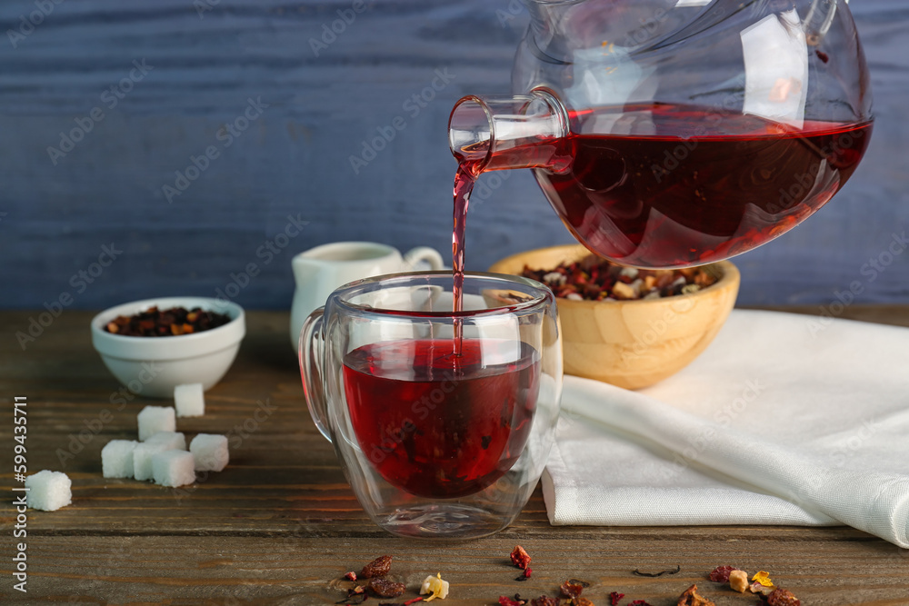 Pouring of fruit tea from teapot into glass on wooden table