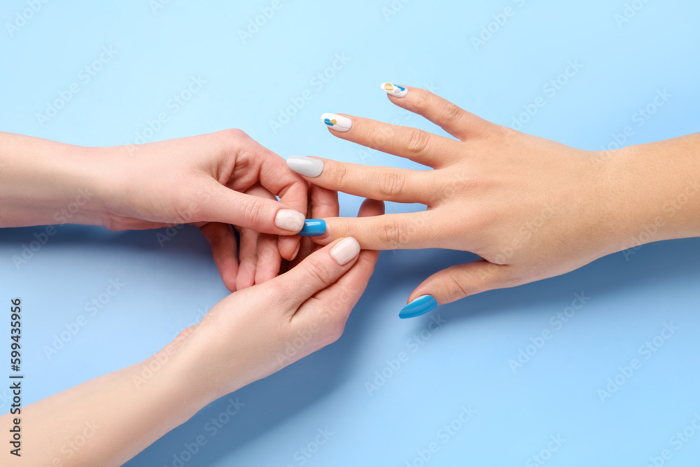 Manicure master applying press-on nail on blue background, closeup