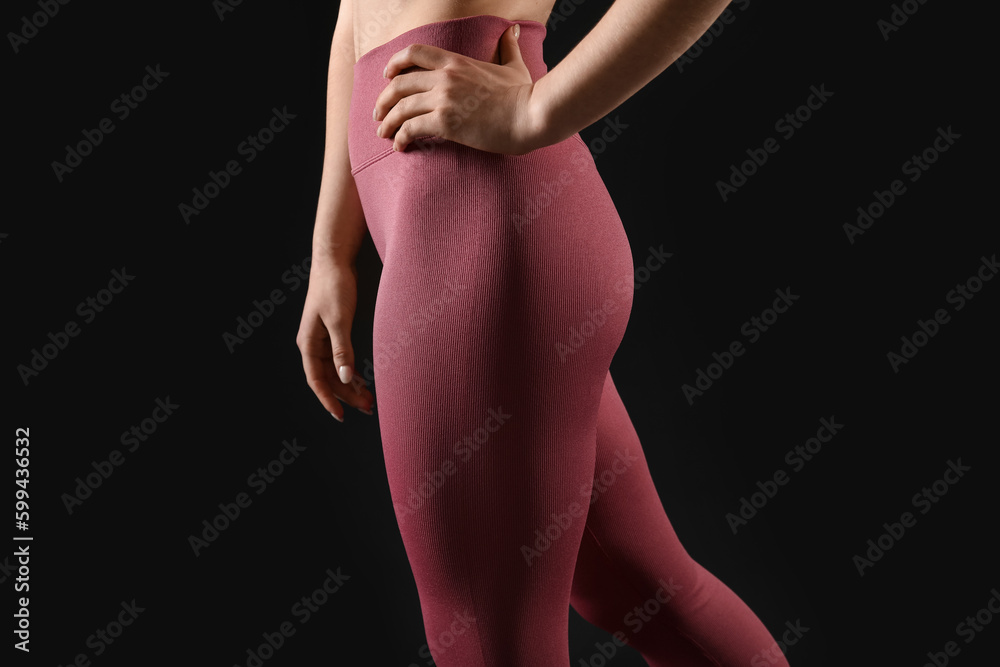 Sporty young woman in leggings on black background, closeup