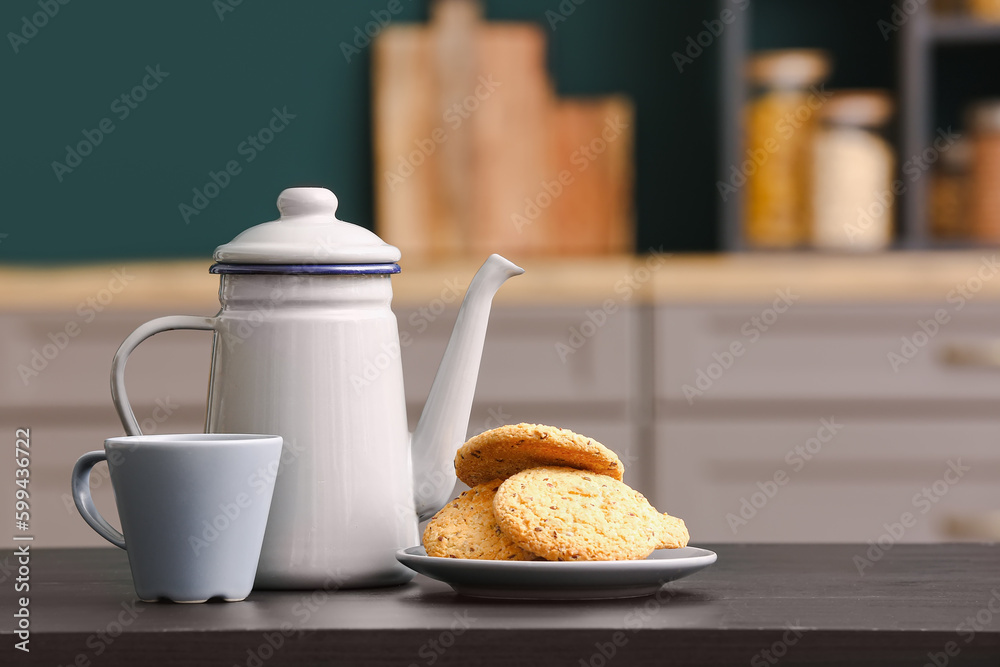 Teapot, cup and plate with cookies on black table in kitchen