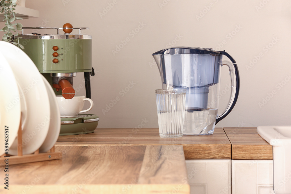 Glass of pure water and filter jug on wooden kitchen counter