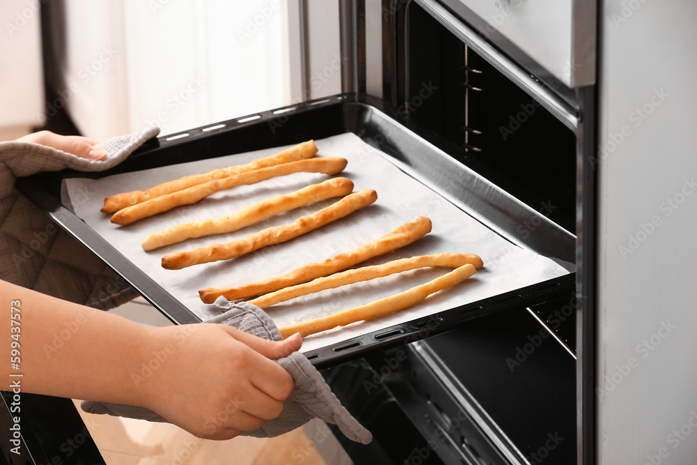 Woman pulling baking tray with prepared Italian Grissini from oven