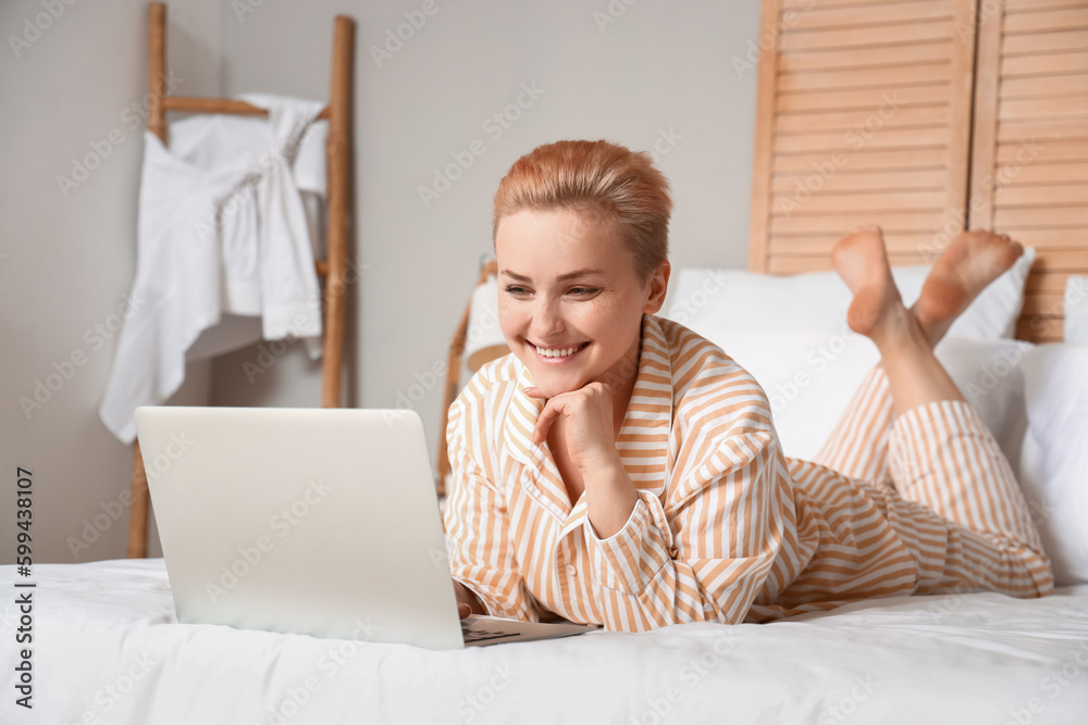 Young woman using laptop on bed in morning