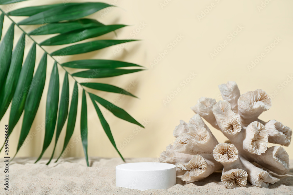 Decorative plaster podium, coral and palm leaves in sand on light background