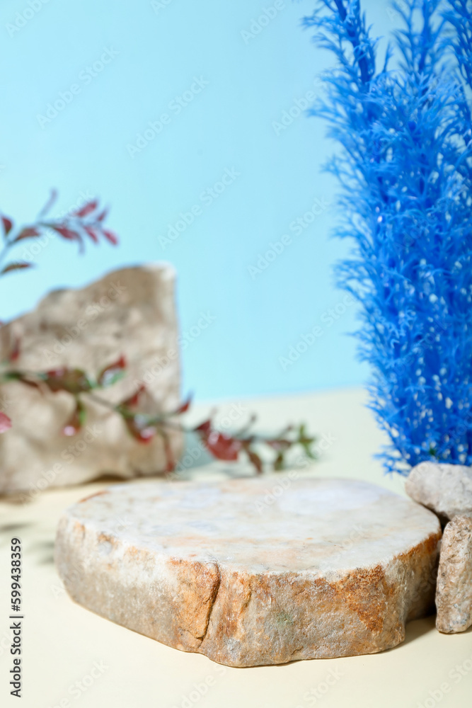 Decorative stone podium and seaweed in sand on blue background