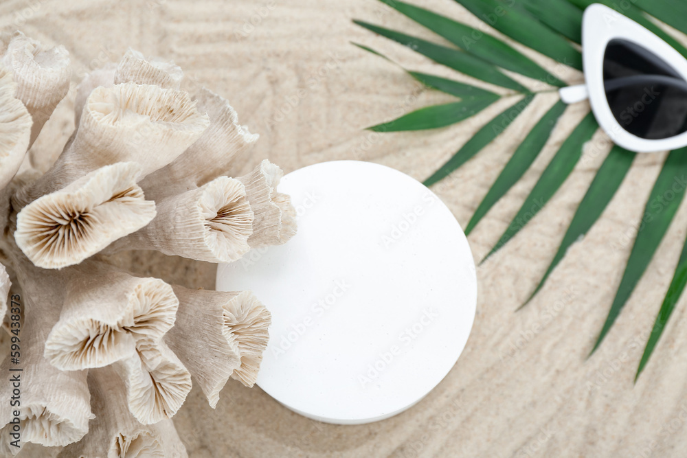 Decorative plaster podium, coral, sunglasses and palm leaves in sand