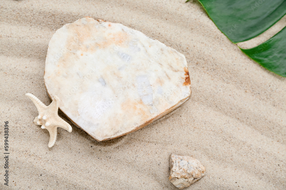 Decorative stone podium, starfish and tropical leaf in sand