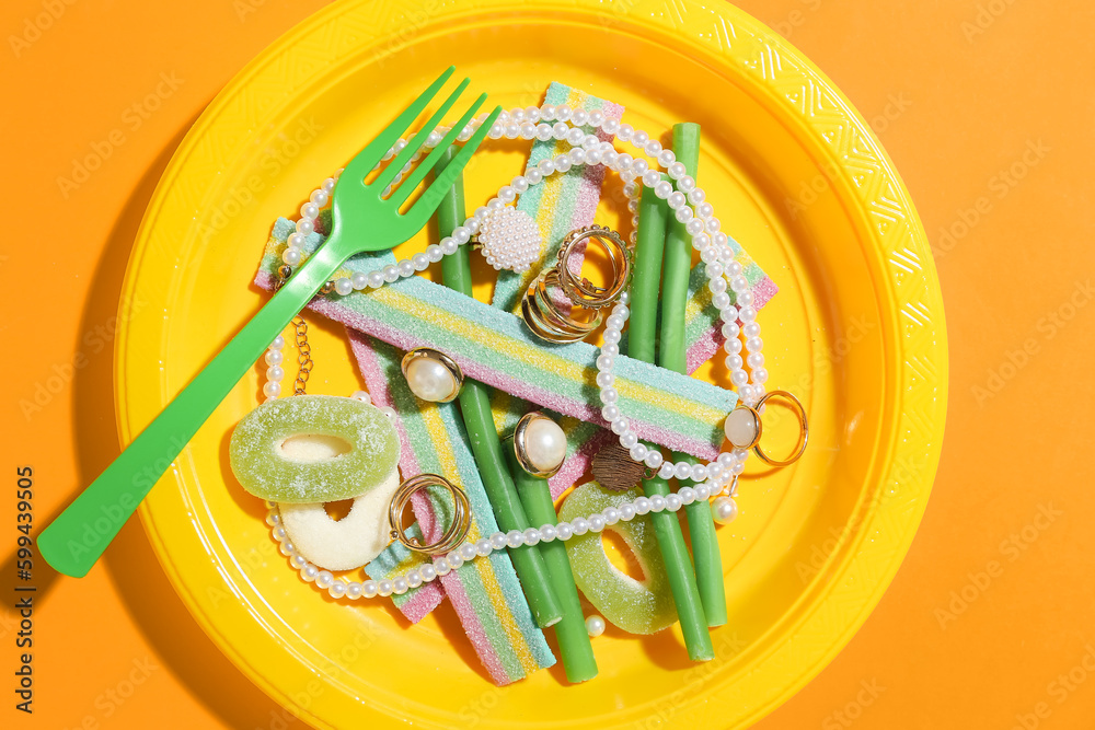 Plate with jelly candies and jewelry on color background, closeup