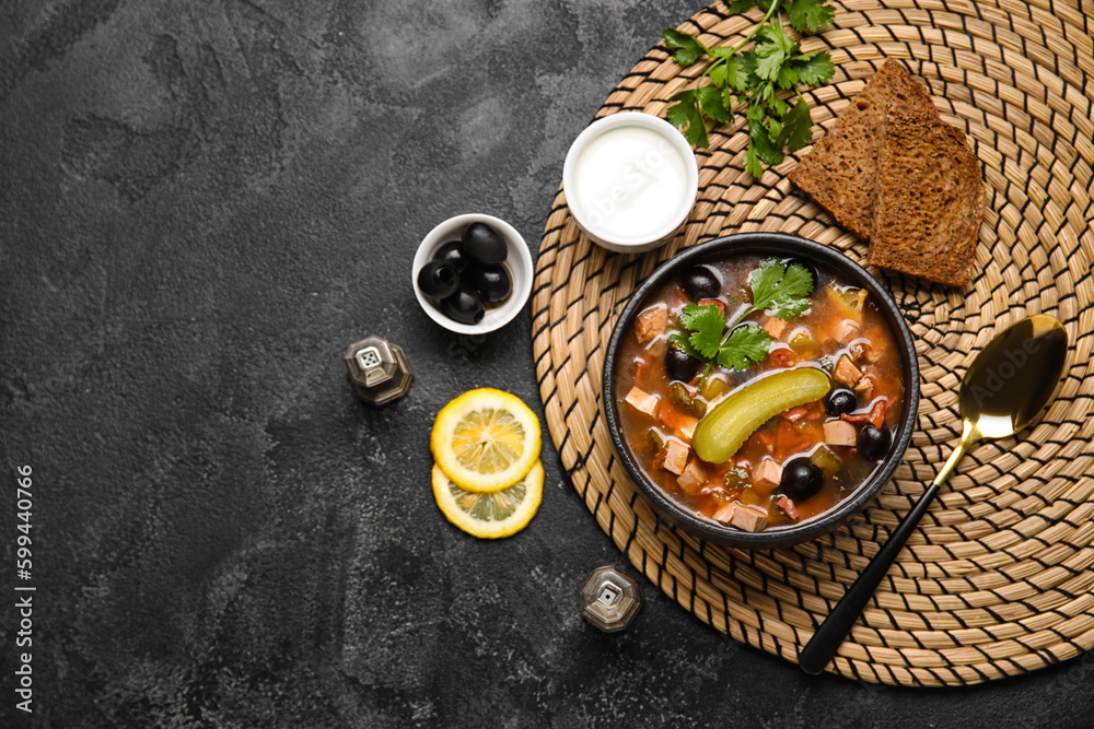 Bowl of tasty Hodgepodge soup with bread and sour cream on dark background