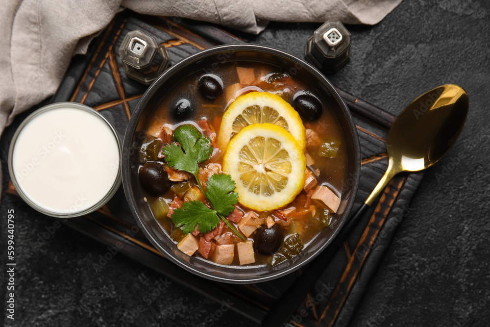 Bowl of tasty Hodgepodge soup with sour cream on dark background