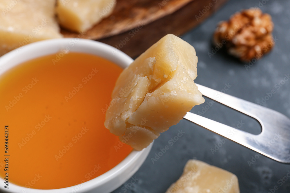 Fork with piece of tasty Parmesan cheese and honey on table, closeup