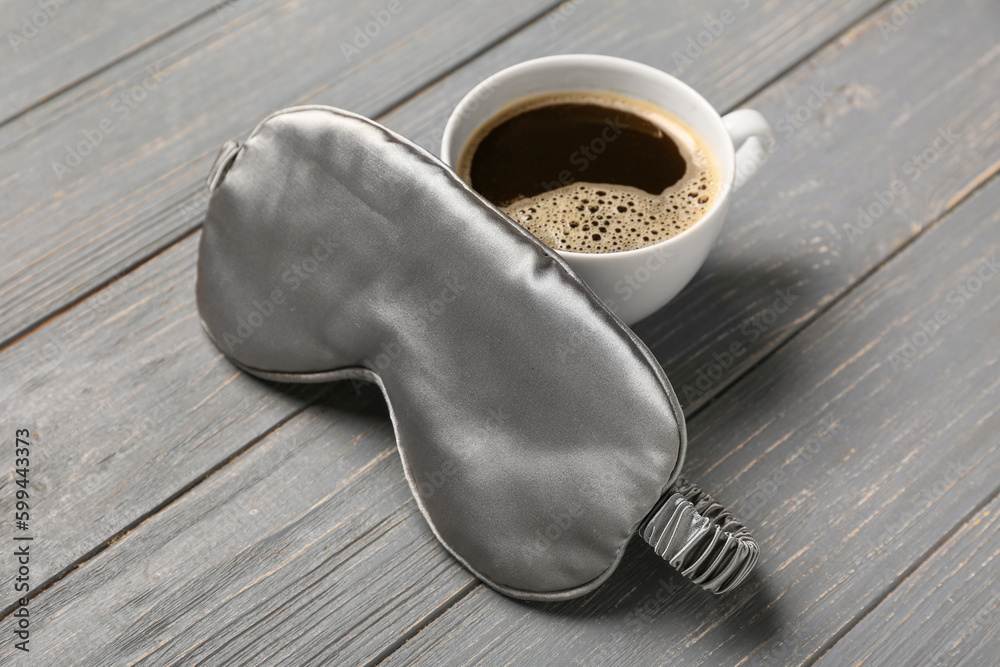 Sleep mask and cup of coffee on grey wooden background