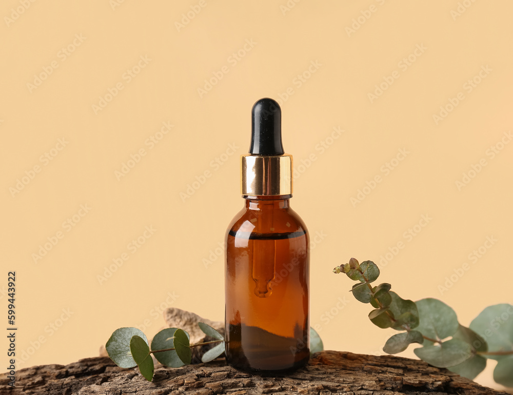 Bottle of cosmetic oil with eucalyptus branches and tree bark on pale yellow background