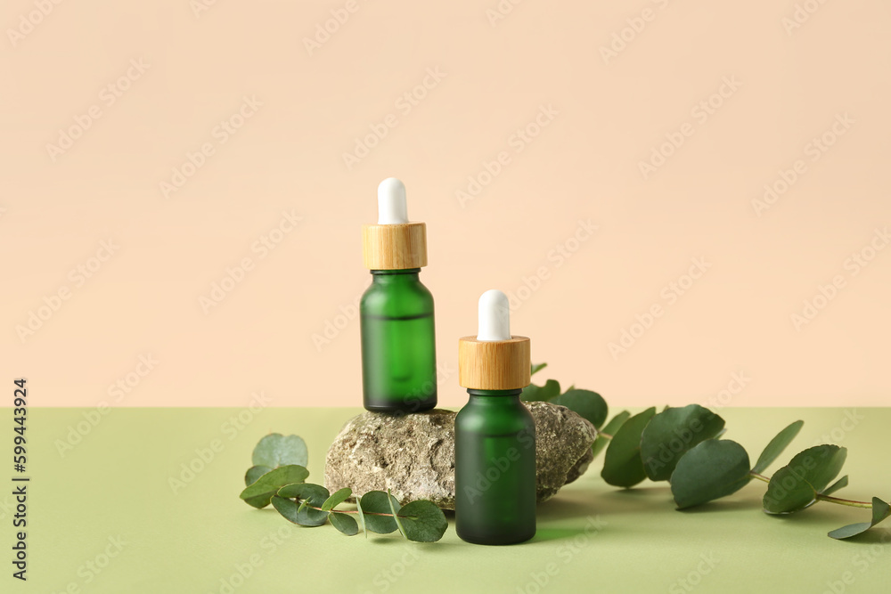 Bottles of cosmetic oil with eucalyptus branches and stone on green table