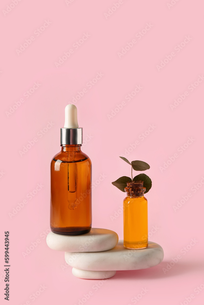 Bottles of cosmetic oil with stones on pink background