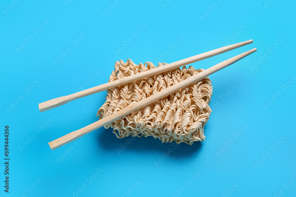 Raw instant noodles and wooden chopsticks on blue background