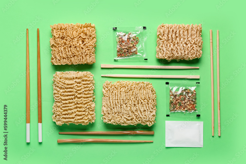 Composition of raw instant noodles with wooden chopsticks and seasoning on light green background