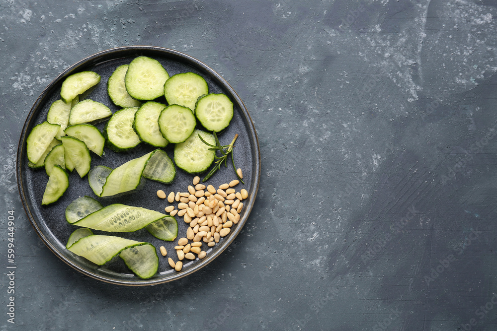 Plate with pieces of fresh cucumber and nuts on green background