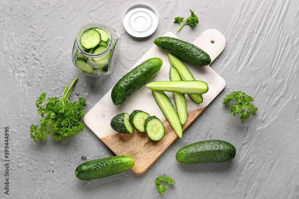 Board and jar with fresh cucumbers on grey background