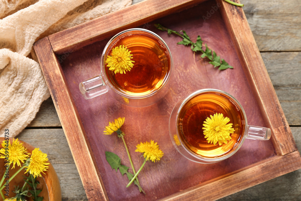 Board with glass cups of healthy dandelion tea on wooden background