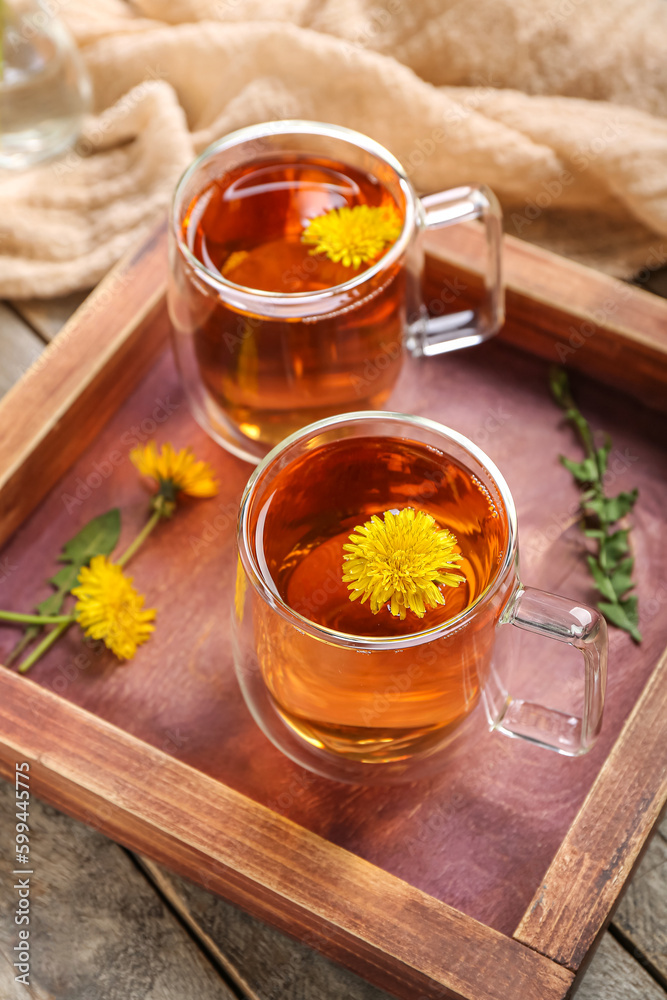 Board with glass cups of healthy dandelion tea on wooden background