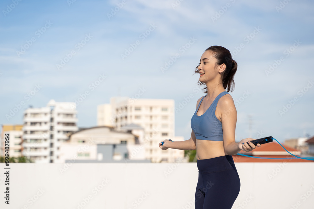 Young Asian woman with jump rope on rooftop. Fitness female doing skipping workout outdoors