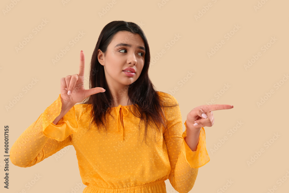 Young woman showing loser gesture on beige background