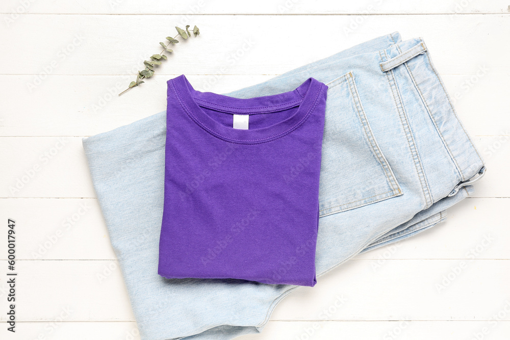 Folded t-shirt and jeans with eucalyptus branch on white wooden background