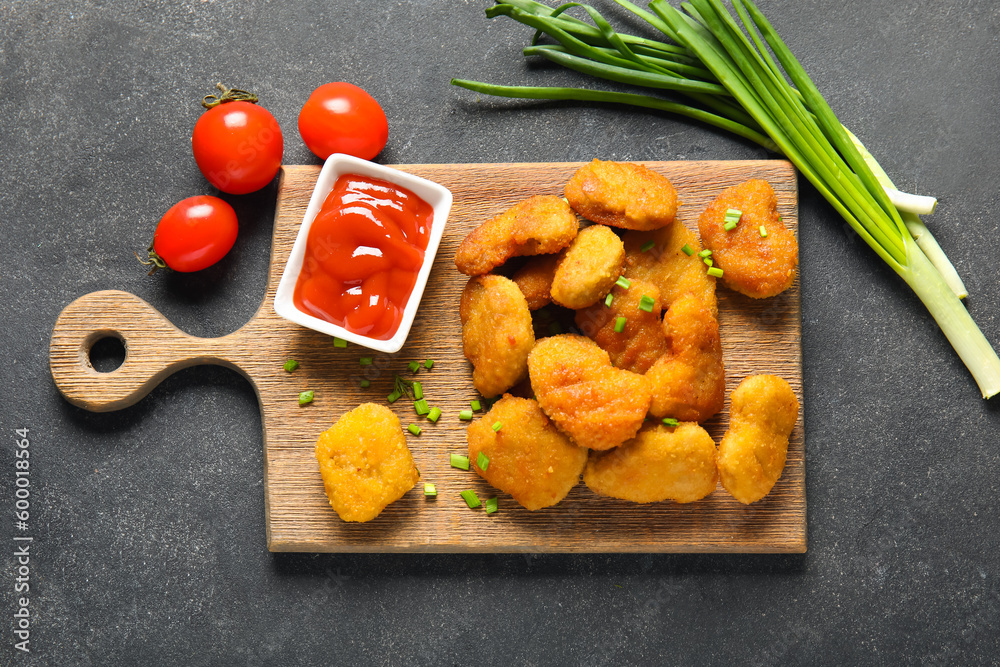 Board with delicious nuggets, ketchup and vegetables on black table