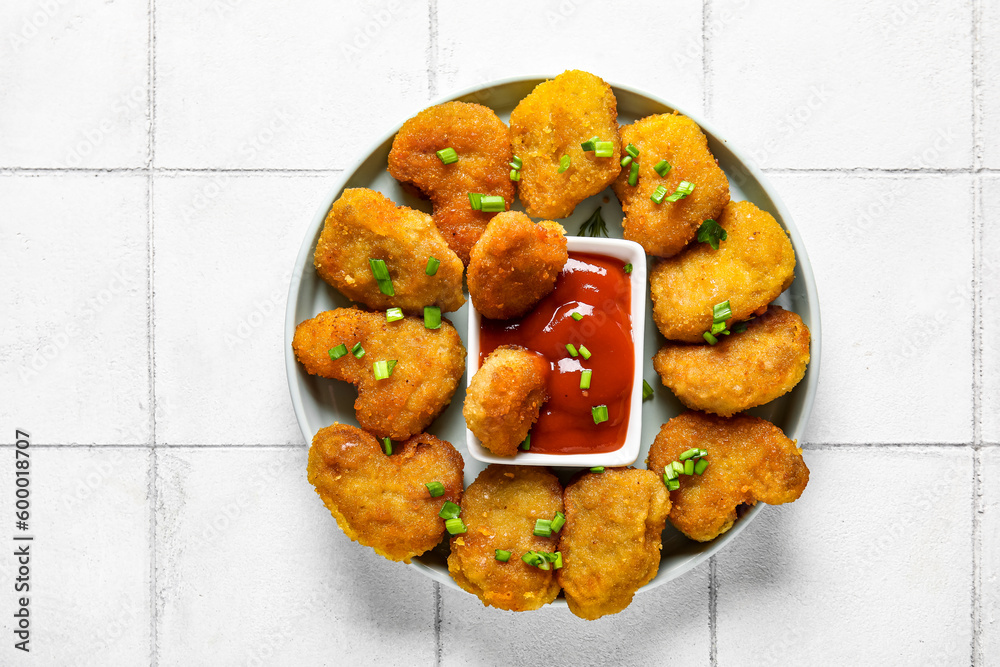 Plate with delicious nuggets, bowl of ketchup and cut green onion on white tiled table