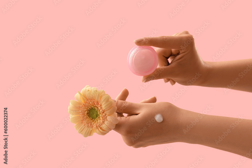 Hands holding jar of cream and flower on pink background