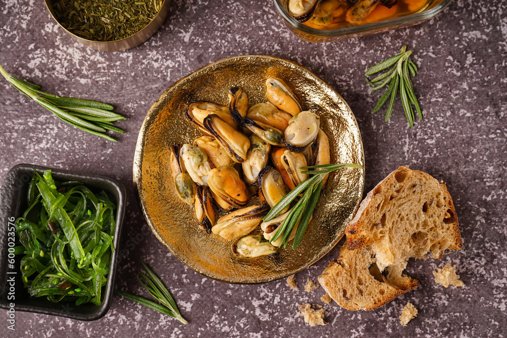 Plate with pickled mussels and bowl of seaweed salad on dark background