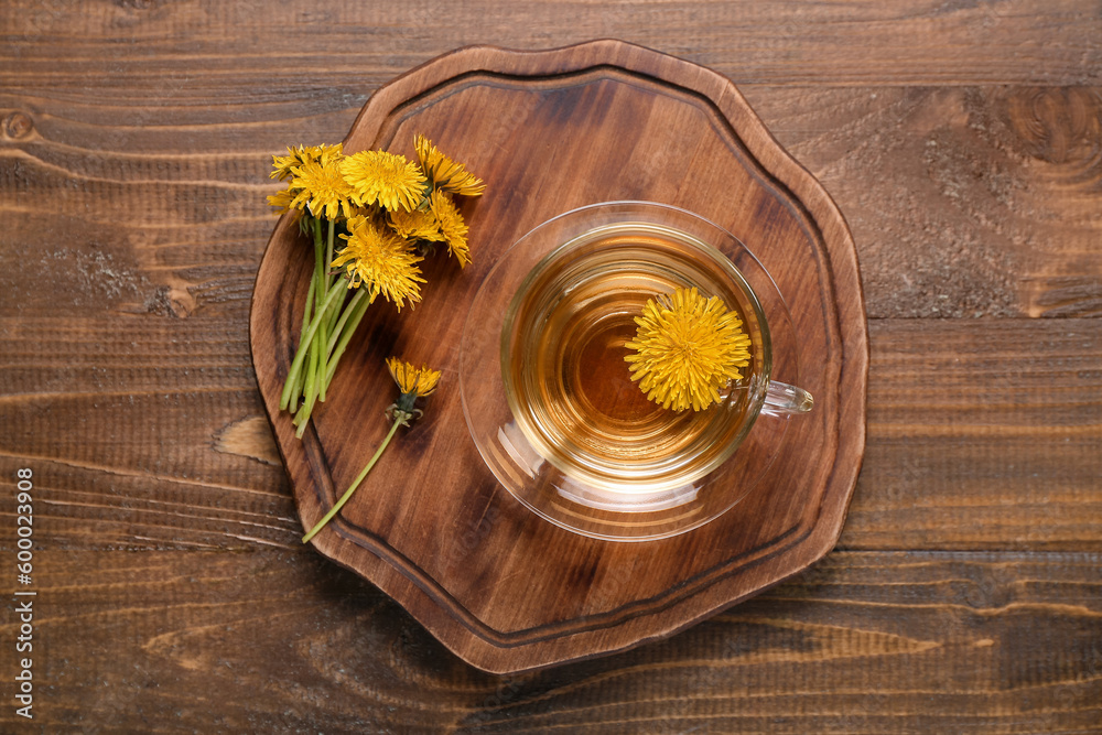 Board with glass cup of healthy dandelion tea on wooden background