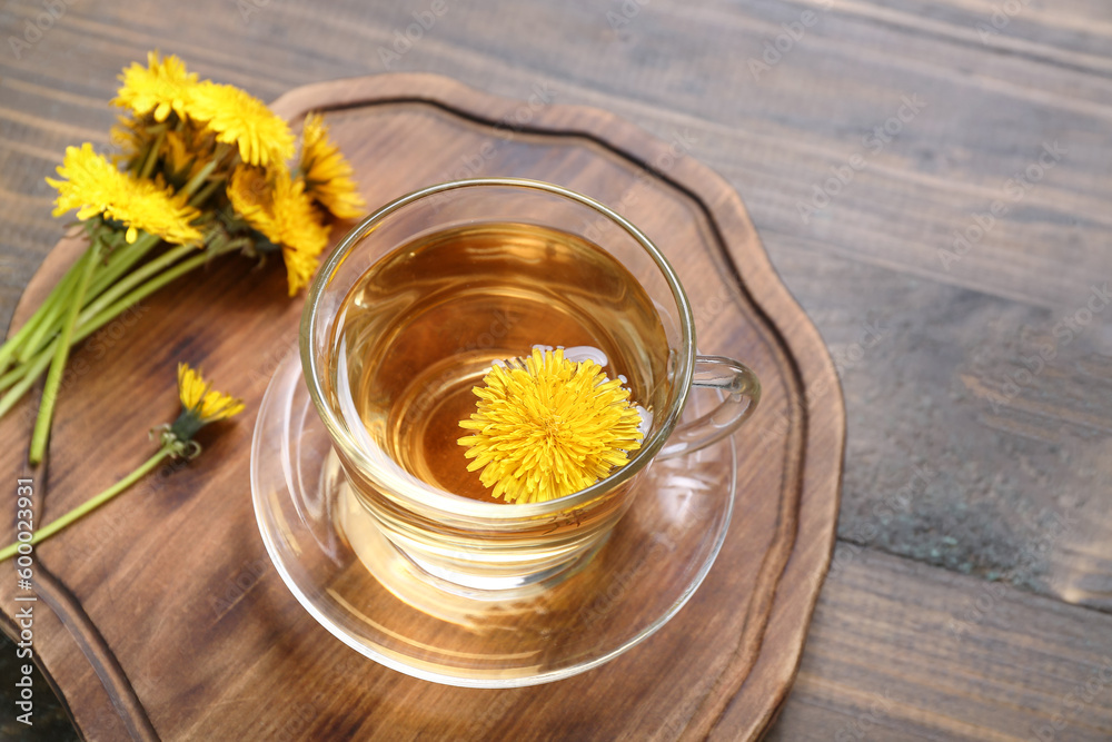 Board with glass cup of healthy dandelion tea on wooden background