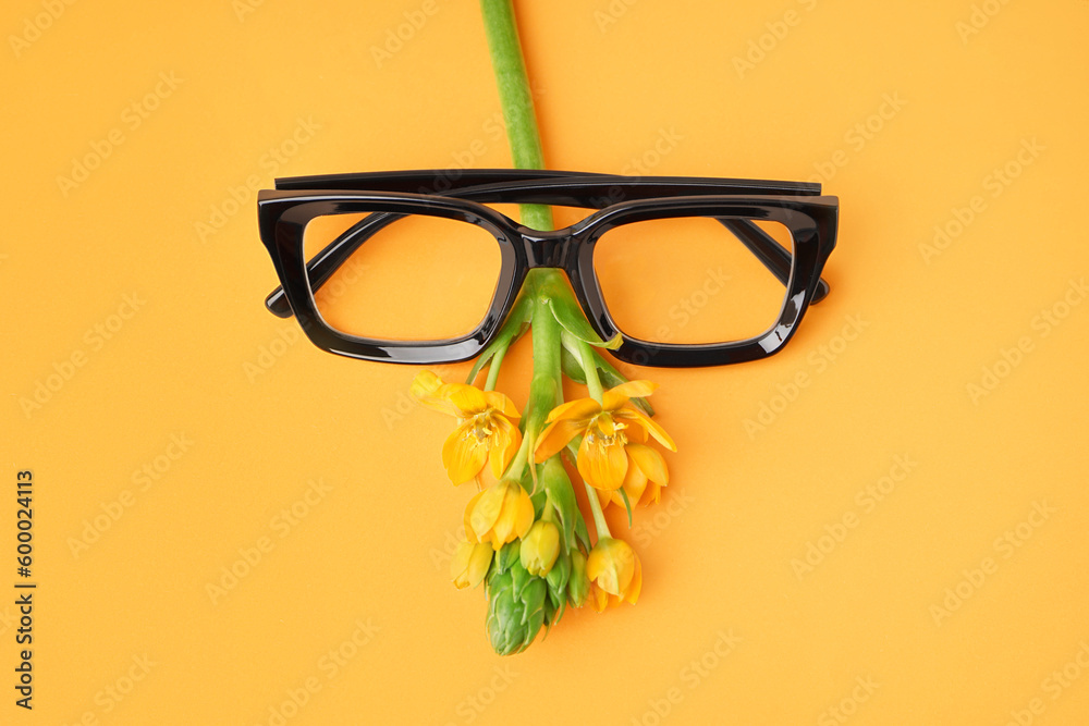 Stylish eyeglasses and flower on yellow background