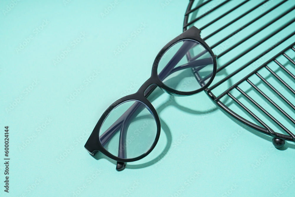 Black modern eyeglasses and stand on pale turquoise background