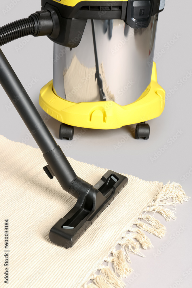 Vacuum cleaner with rug on grey background, closeup