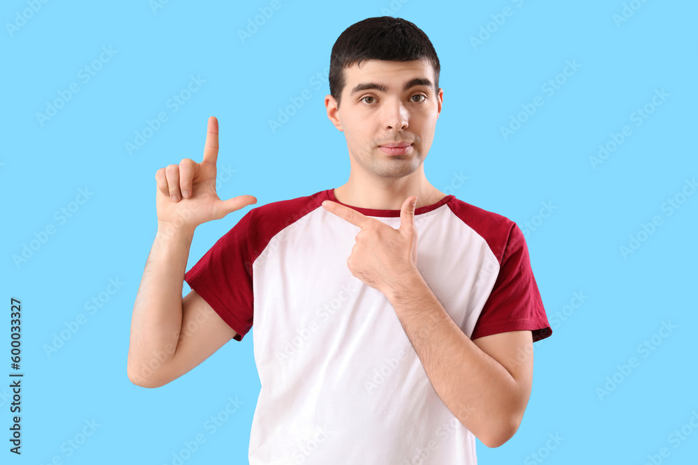 Young man showing loser gesture on blue background