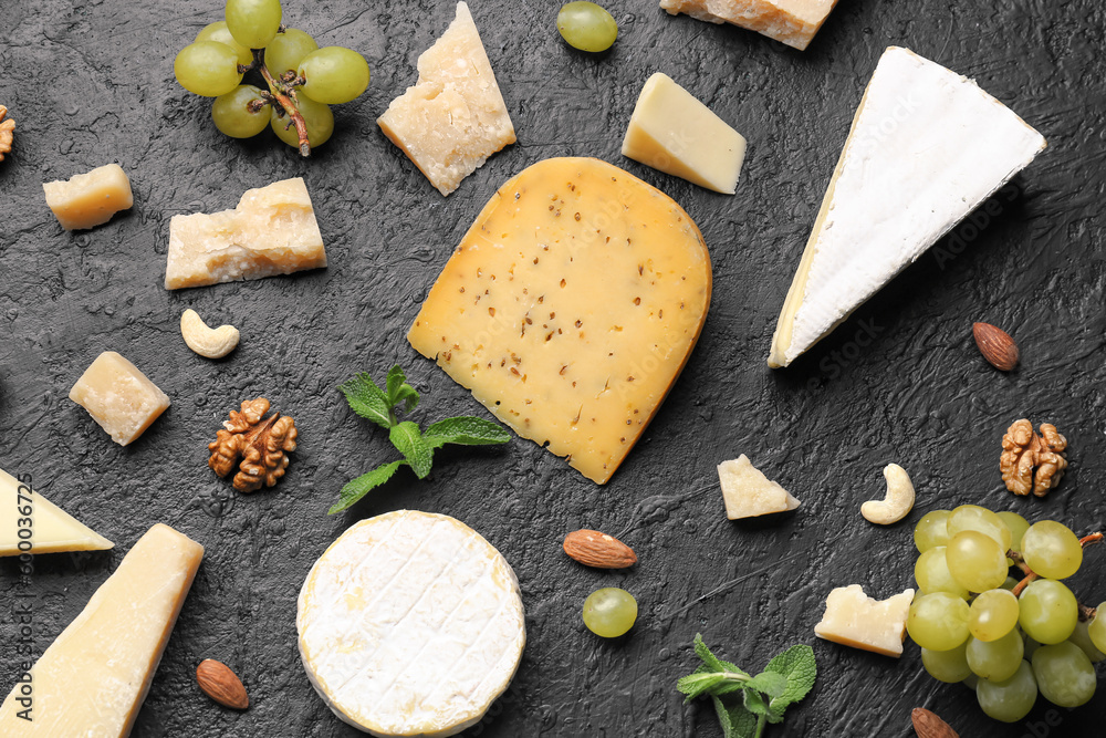 Different types of tasty cheese, grapes and nuts on dark background