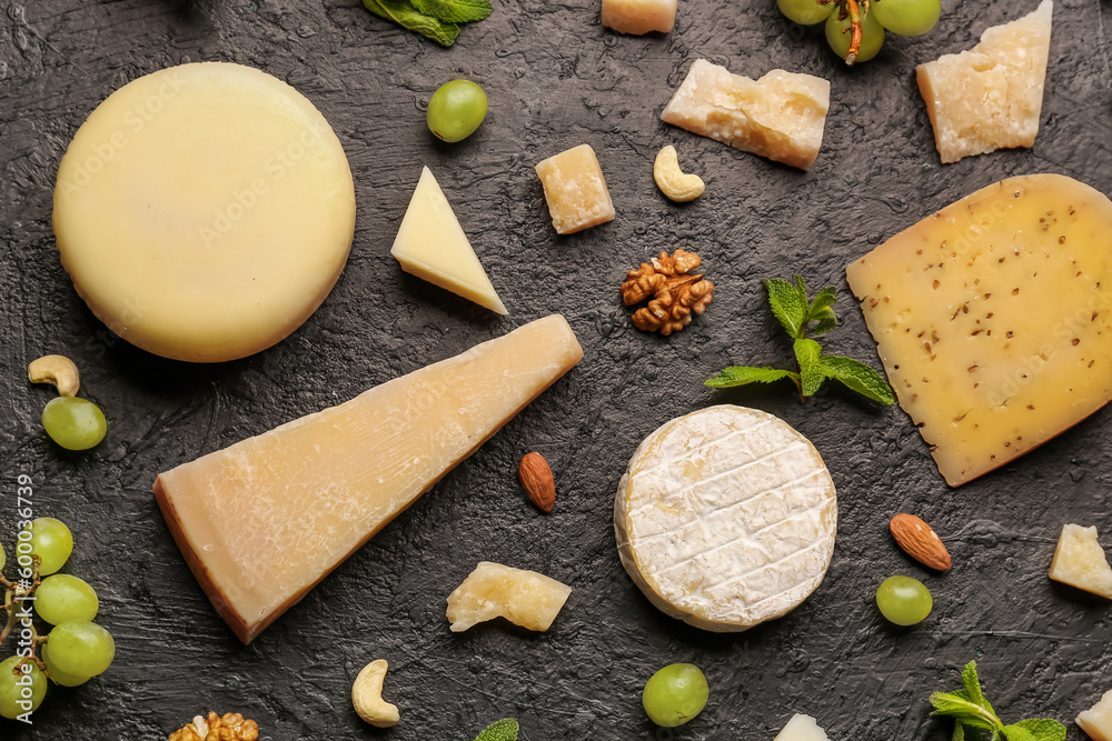 Different types of tasty cheese, grapes and nuts on dark background