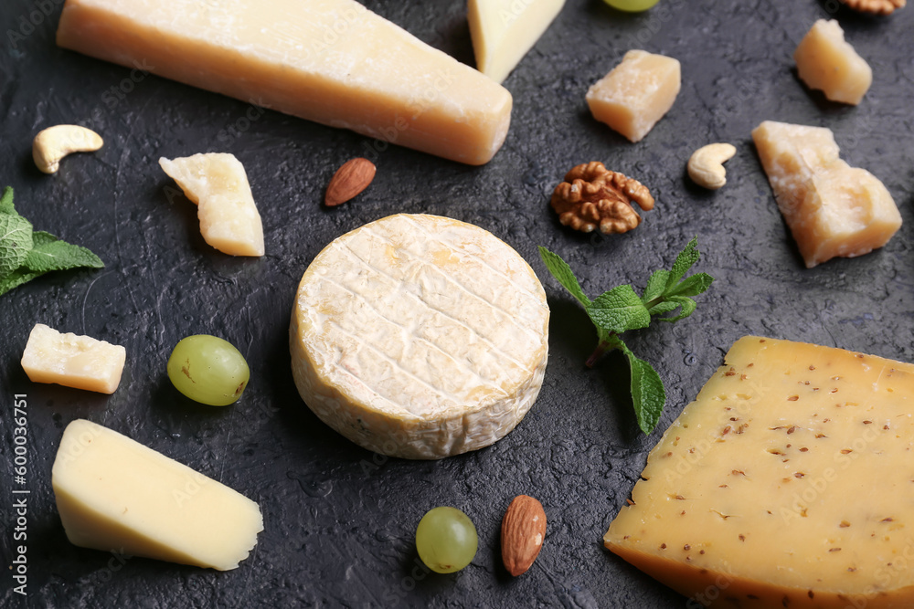 Different types of tasty cheese, grapes and nuts on dark background