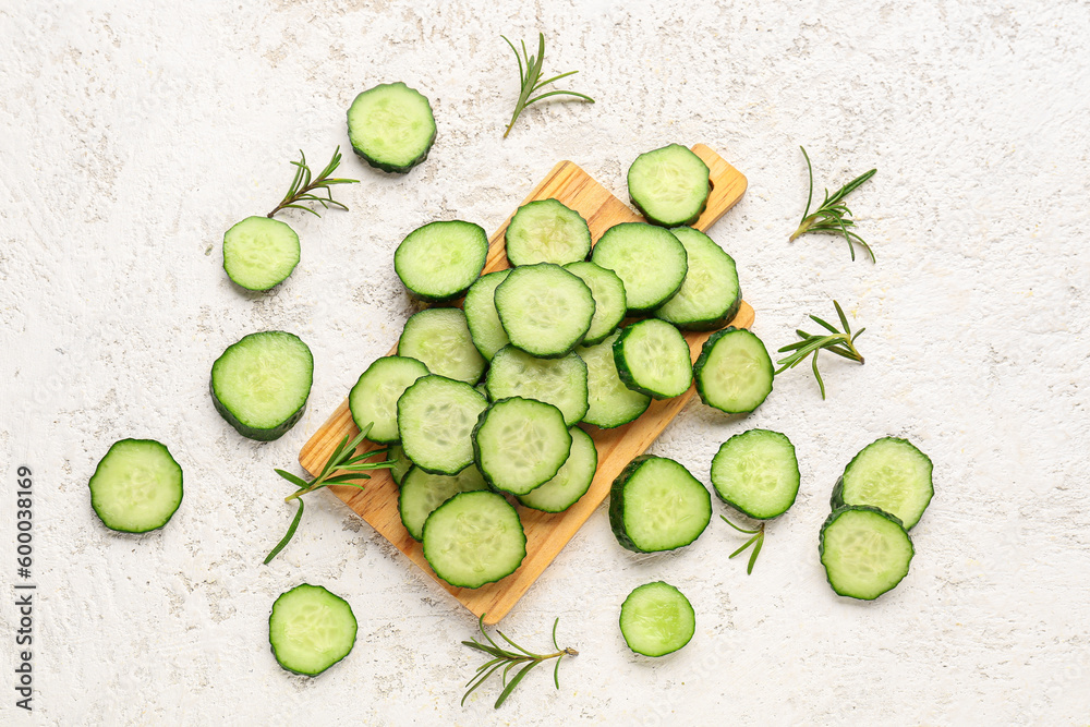 Wooden board with pieces of fresh cucumber on light background