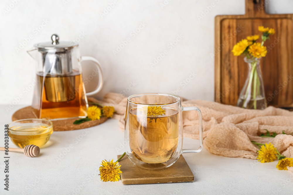 Glass cup of healthy dandelion tea and teapot on white table