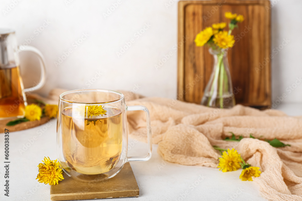 Glass cup of healthy dandelion tea and teapot on white table