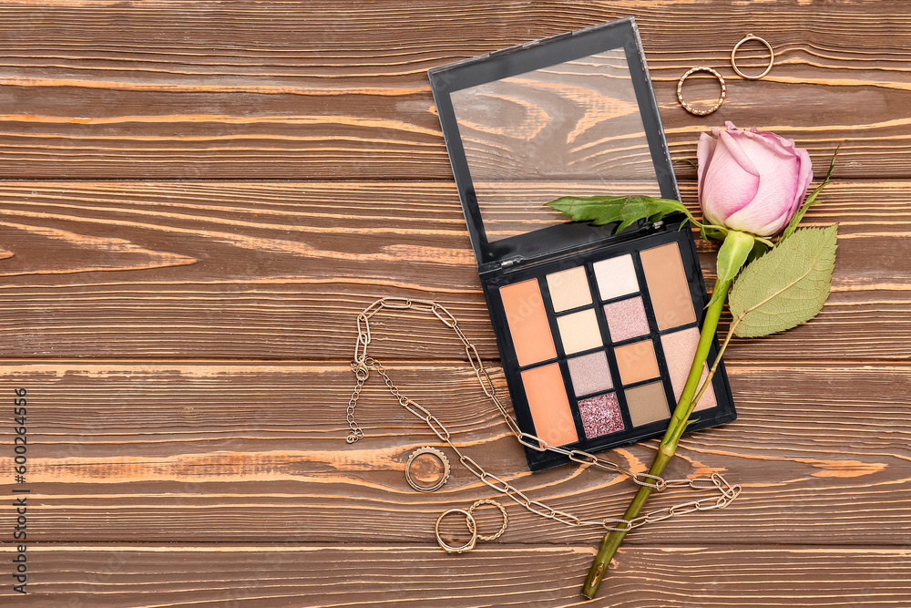 Palette of eyeshadows, beautiful female accessories and rose flower on wooden background